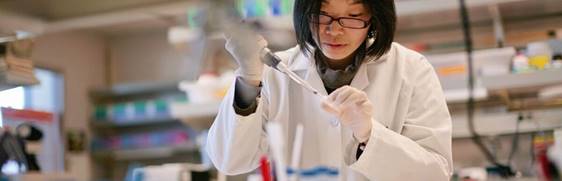 Woman with glasses in a lab inserting fluid into a test tube